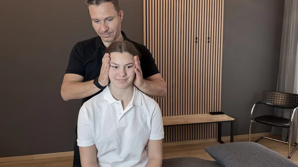 Physiotherapeut behandelt den Kieferbereich einer sitzenden Patientin