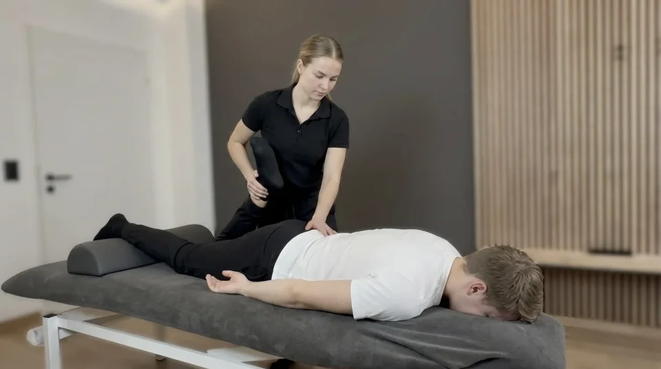 Physiotherapeutin mobilisiert das Bein eines Patienten auf einer Behandlungsliege